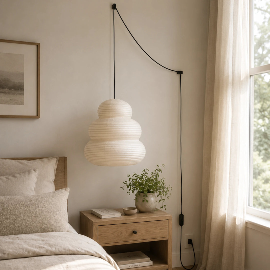 Tiered paper pendant on a swag cord beside a bed with linen bedding