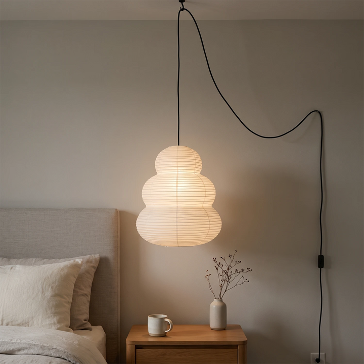 Tiered paper pendant on a swag cord hanging beside a bed