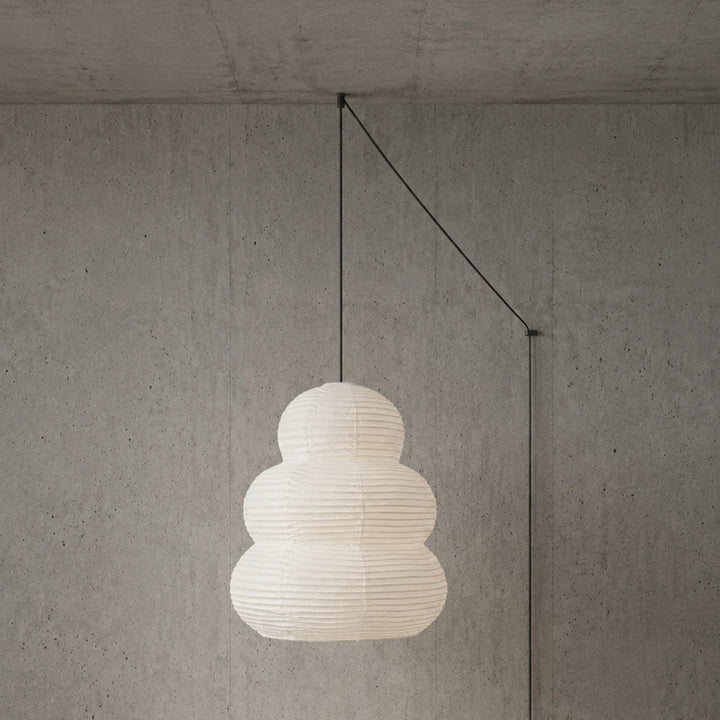 Tiered stacked paper pendant on a black swag cord mounted against a concrete wall