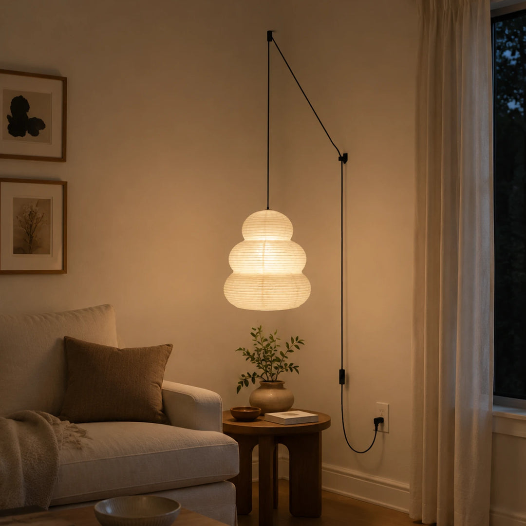 Tiered paper pendant on a swag cord glowing above a reading corner