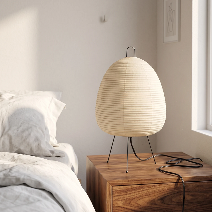 Paper table lamp on a nightstand beside crisp white bedding in a calm bedroom