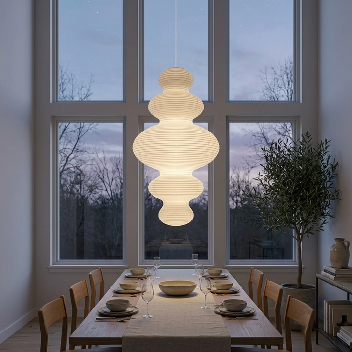 Sculptural paper pendant above a set dining table beside dusk-lit windows