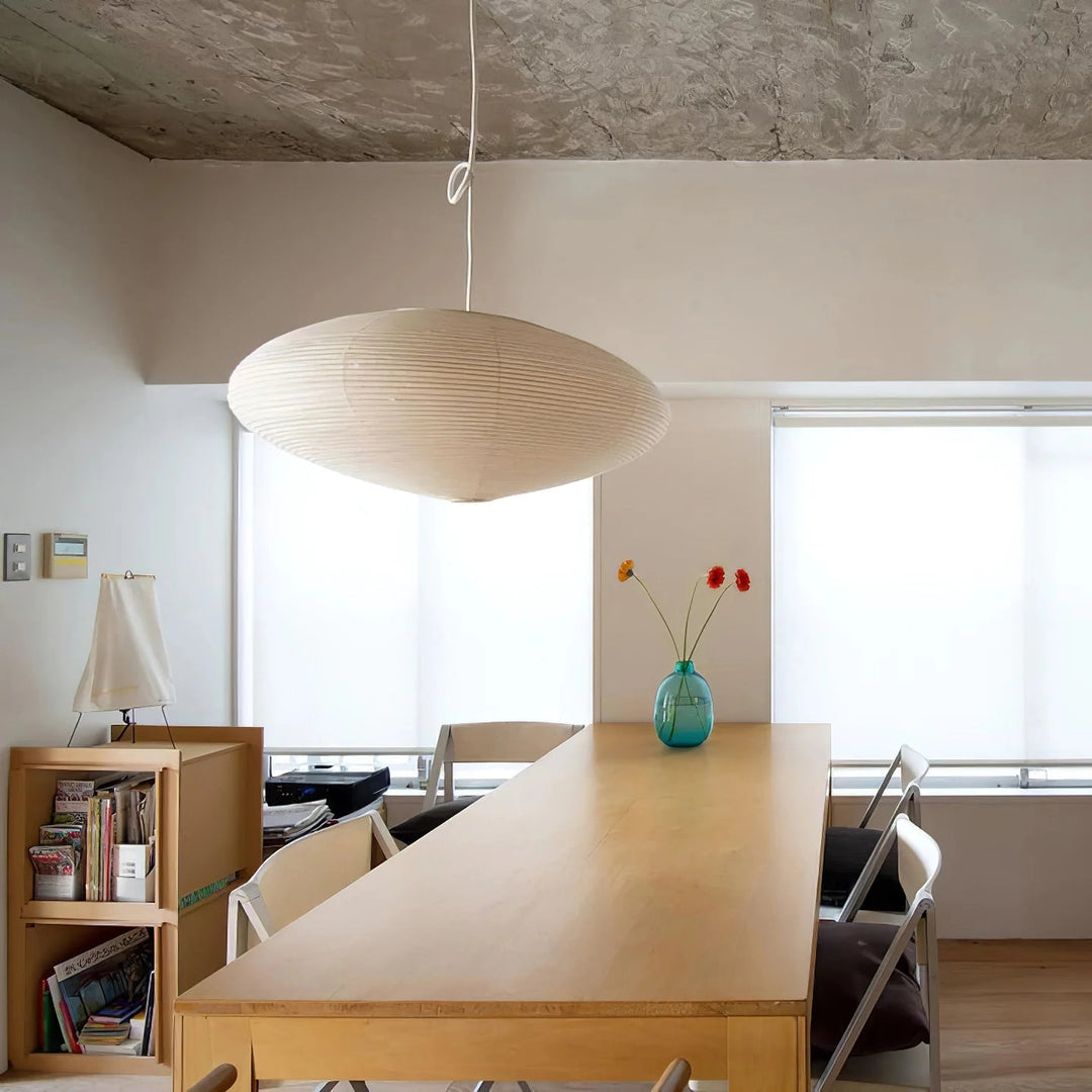 Large oval washi paper pendant light above extra long wooden work table beside tall windows