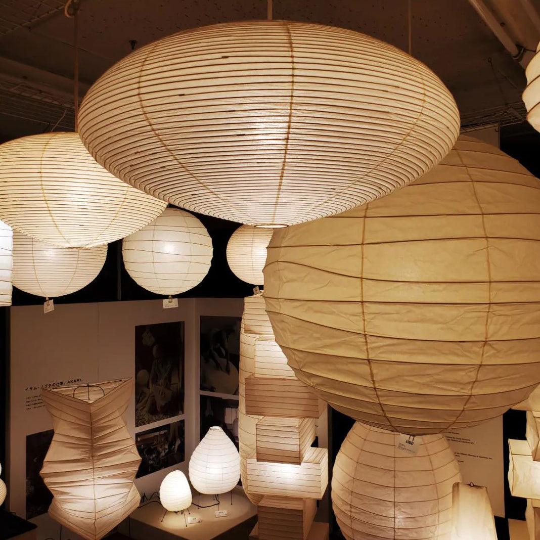 Multi-size washi paper oval and spherical pendant lights displayed together inside lighting showroom, warm illuminated display scene