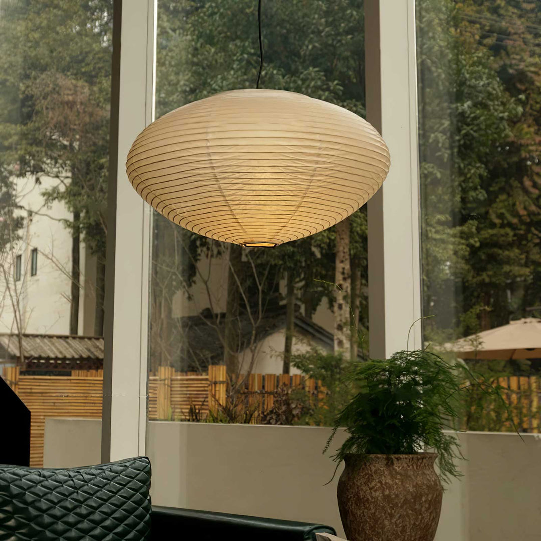 Oval washi paper pendant hanging beside large floor window with lush outdoor green scenery view