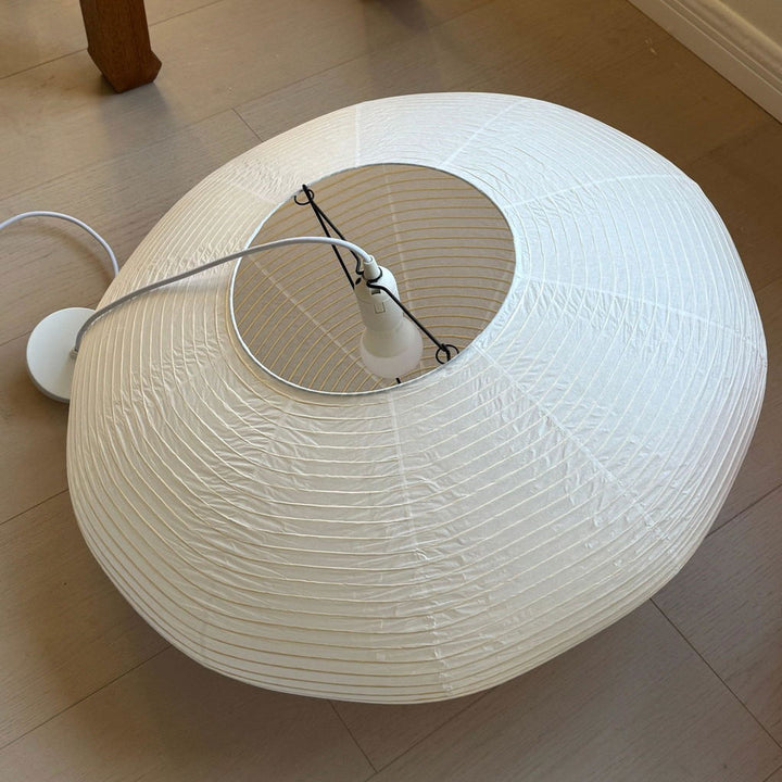White oval washi paper lampshade laid flat on tile floor, showing opening and internal hanging hardware