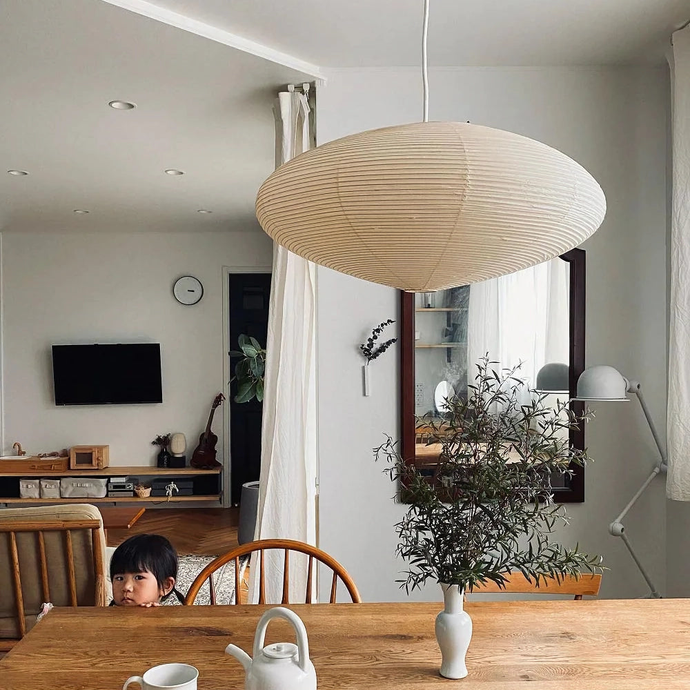 Soft lit washi paper oval pendant hanging above solid wood dining table in casual family dining space